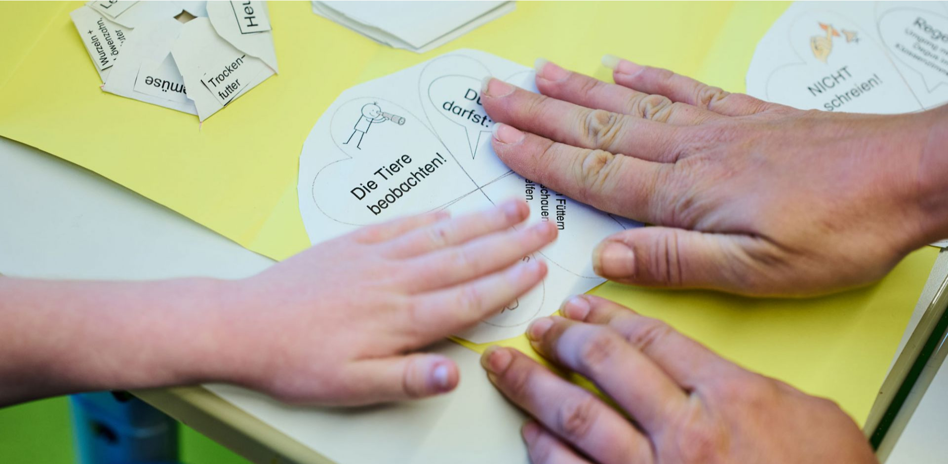 Eine große und eine kleine Hand kleben etwas auf Papier.